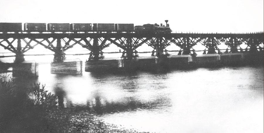 Железнодорожный поезд проходит по мосту, сооруженному на деревянных сваях. Фото. 1900-е.